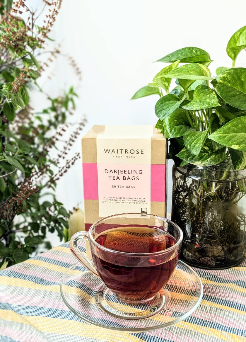 a cup of waitrose darjeeling tea in front of a box of waitrose darjeeling teabags